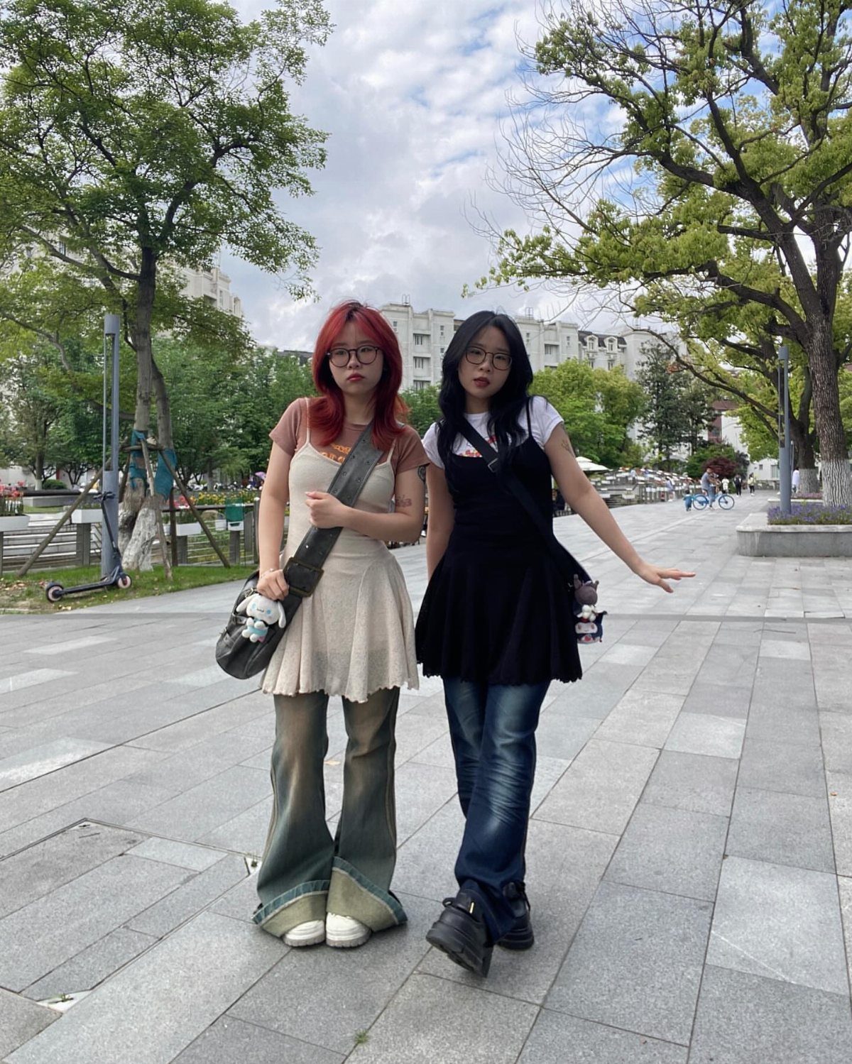 Two women wearing short dresses layered over jeans standing on a city walkway.