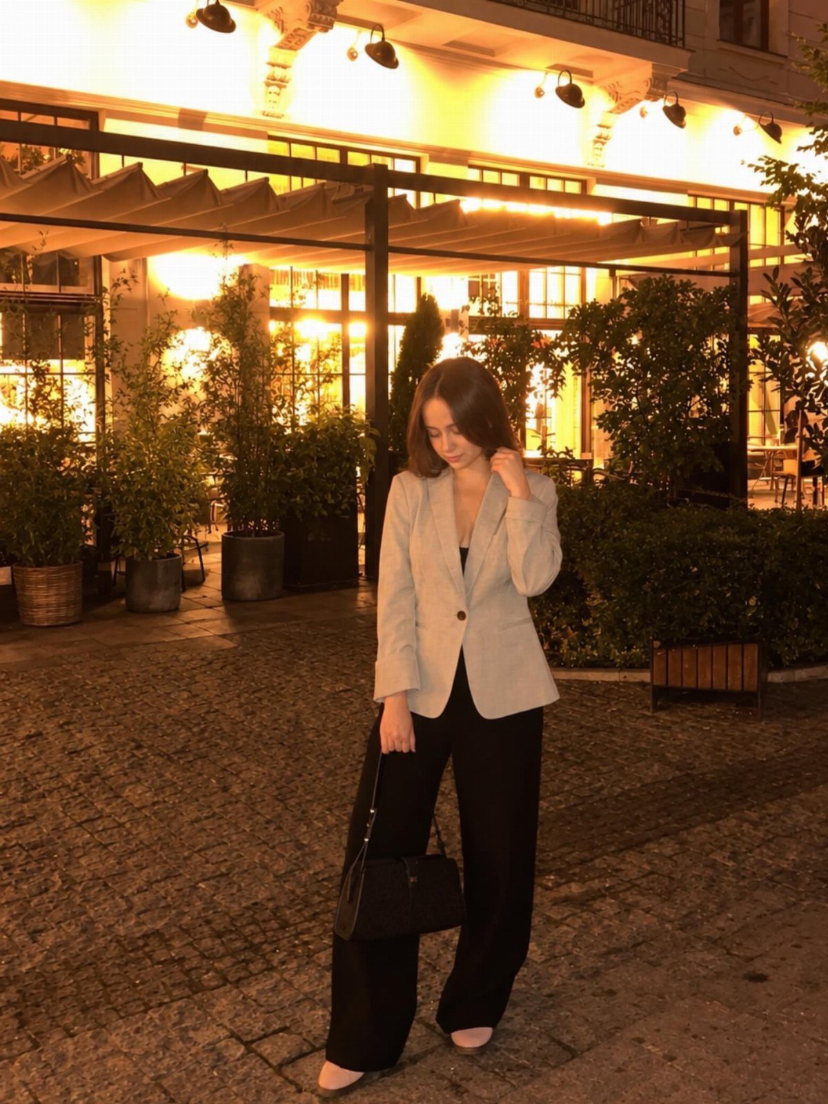 Woman wearing a light blazer and wide-leg black trousers on a cobblestone street.