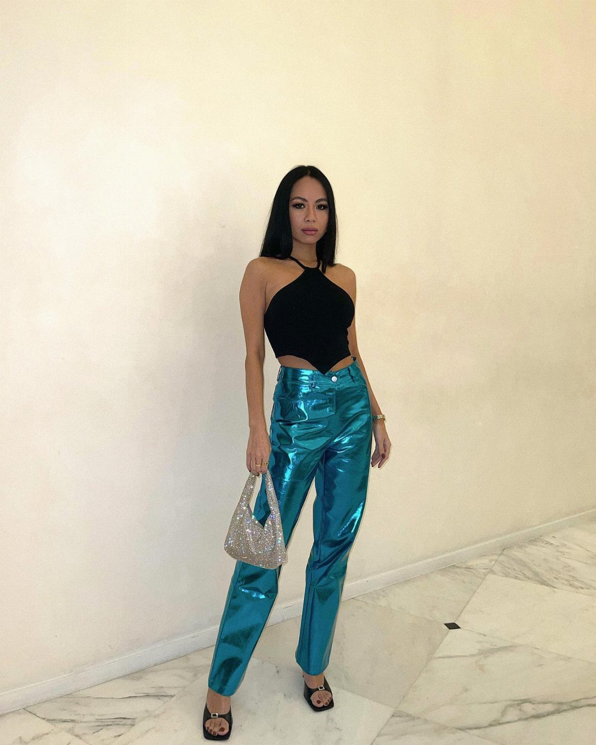 Woman wearing metallic blue pants, a black halter top, and silver glittery handbag.