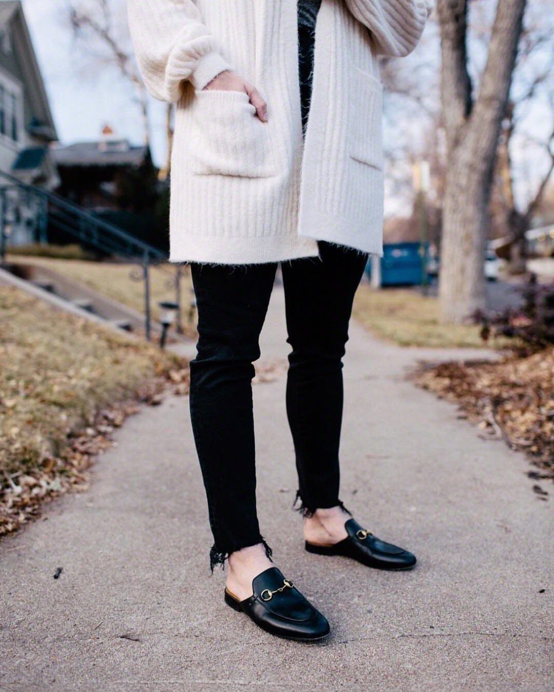 Black leather mules with gold hardware paired with black skinny jeans and white cardigan.