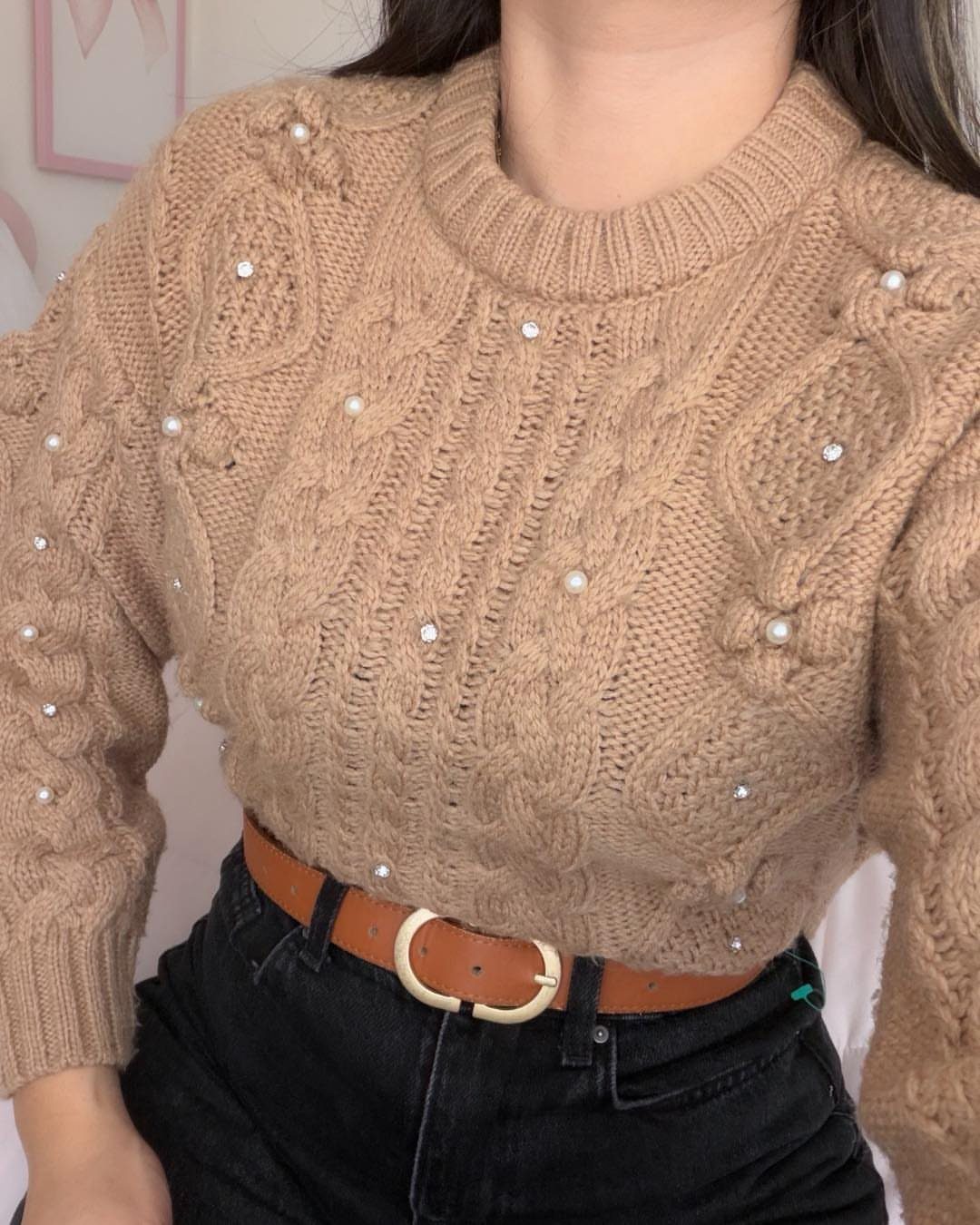 Tan cable-knit sweater with pearl embellishments paired with black jeans and brown belt.