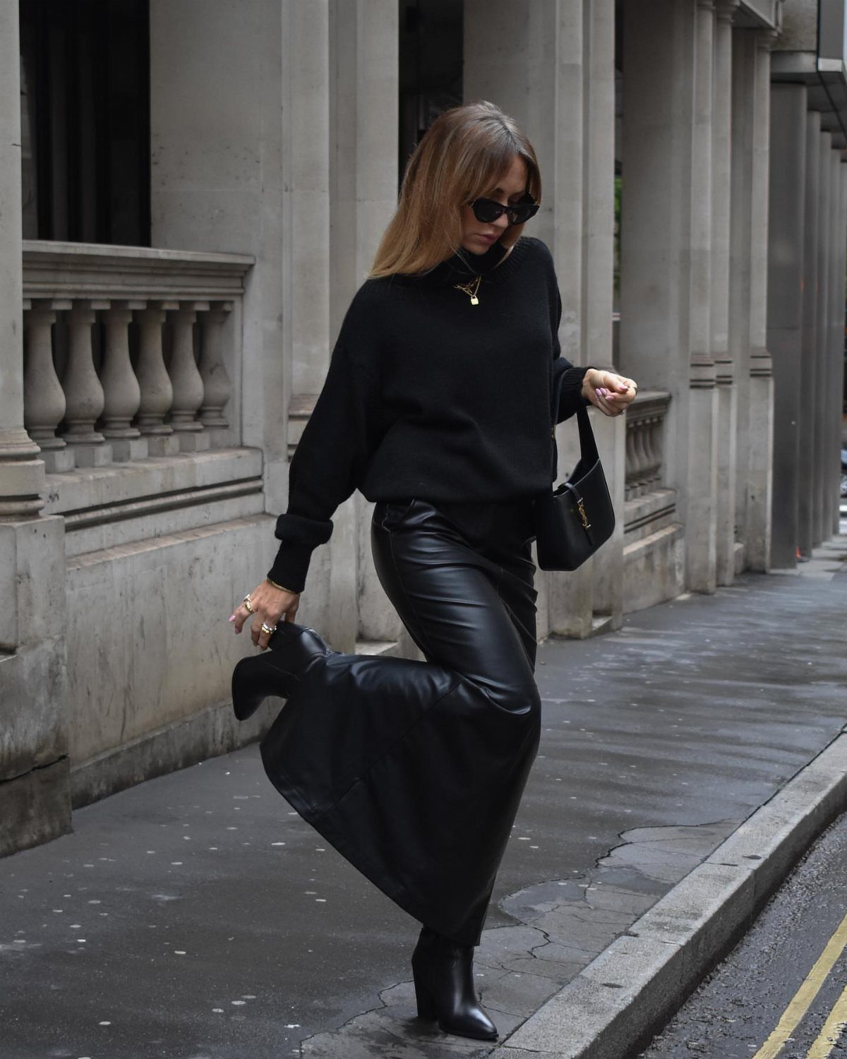 Woman in black sweater and long leather skirt posing on a city street