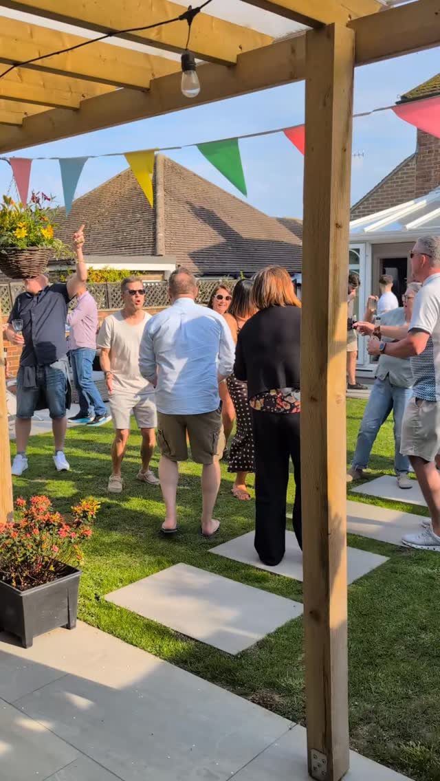 Adults socializing in a sunny backyard garden decorated with colorful bunting and lights.