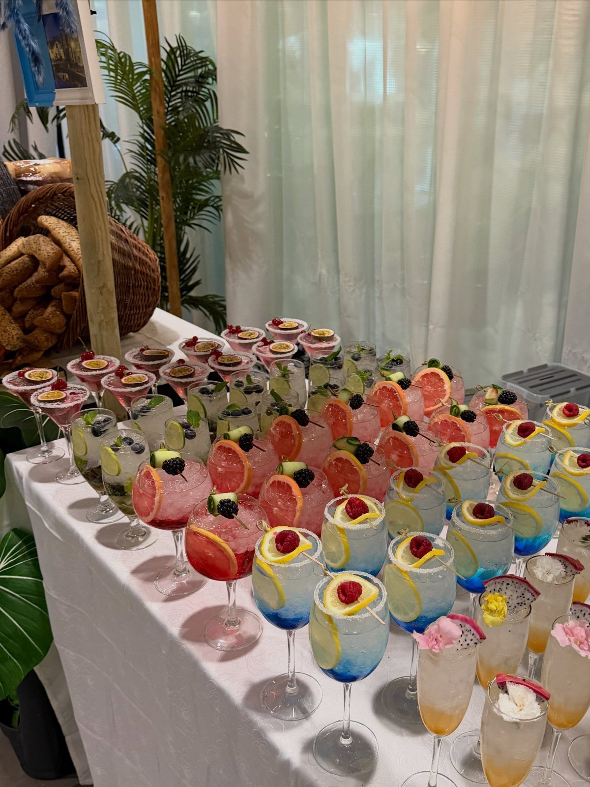 Colorful cocktails and mocktails with fruit garnishes arranged on a white table.