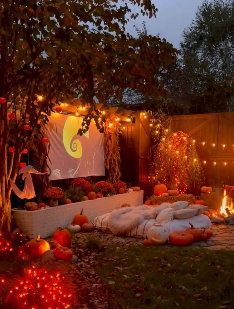 Outdoor movie screen with pumpkins, string lights, and cozy blankets in a backyard