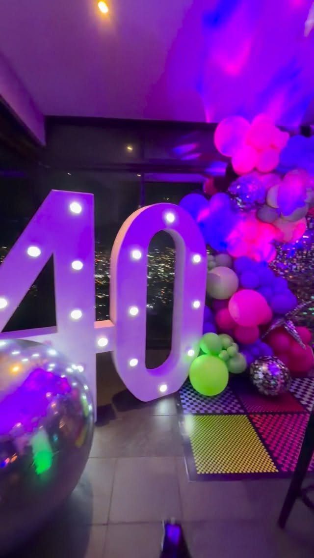Illuminated number 40 with a disco ball and colorful balloons in purple lighting.
