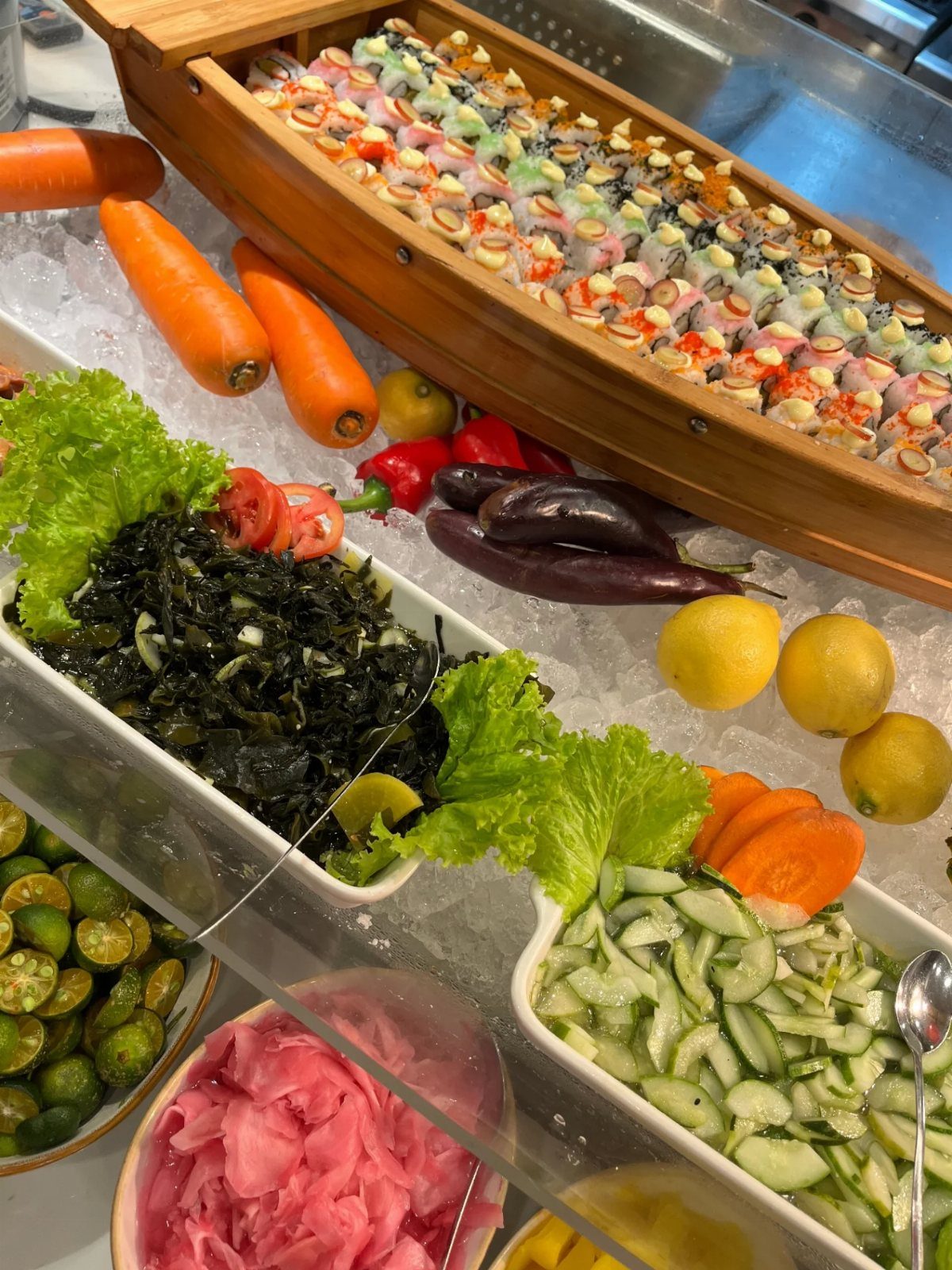 Sushi rolls in a wooden boat surrounded by fresh vegetables on ice.