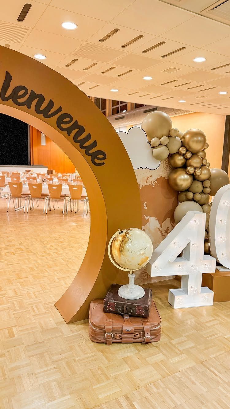 Travel-themed birthday decor with a gold arch, globe, suitcases, and illuminated number 40.