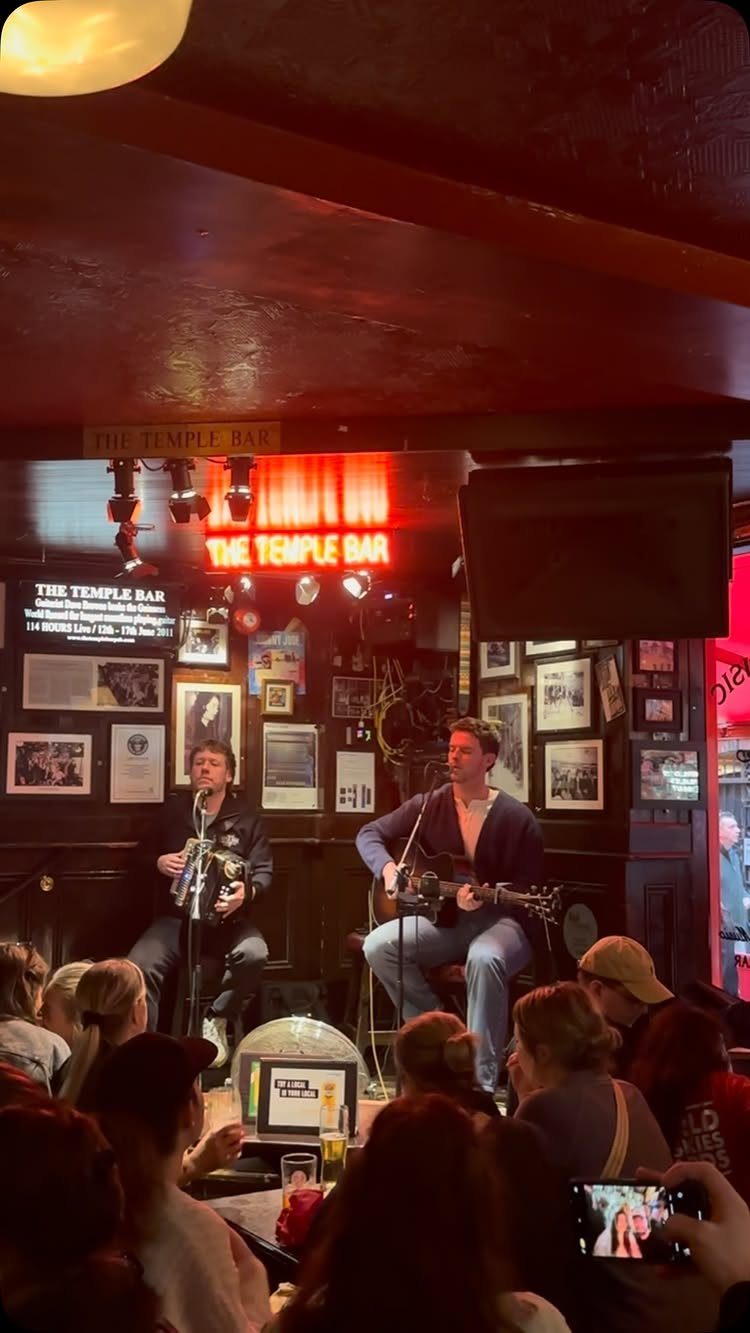 Two musicians playing accordion and guitar for a crowd in a cozy pub.