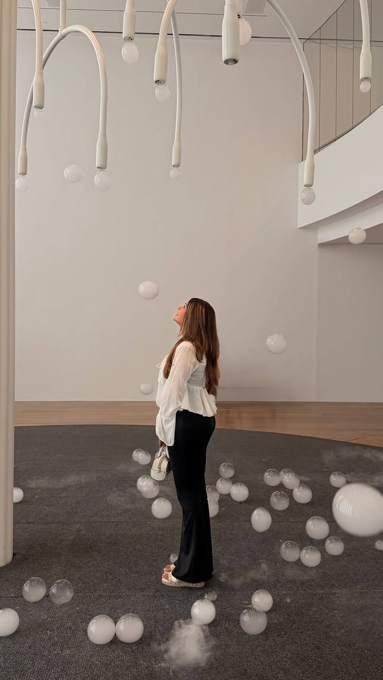 Woman looking up at an art installation with hanging lights and white spheres.