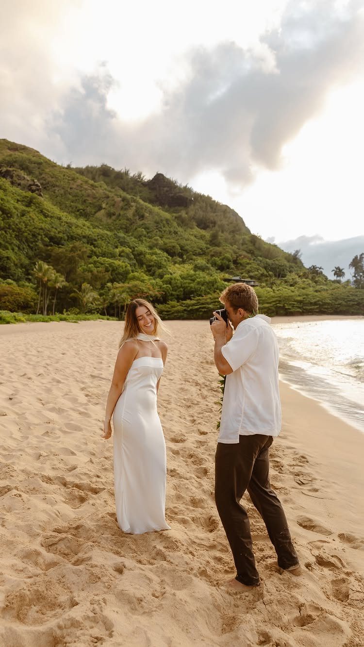 Man photographing a woman in a white dress on a tropical sandy beach