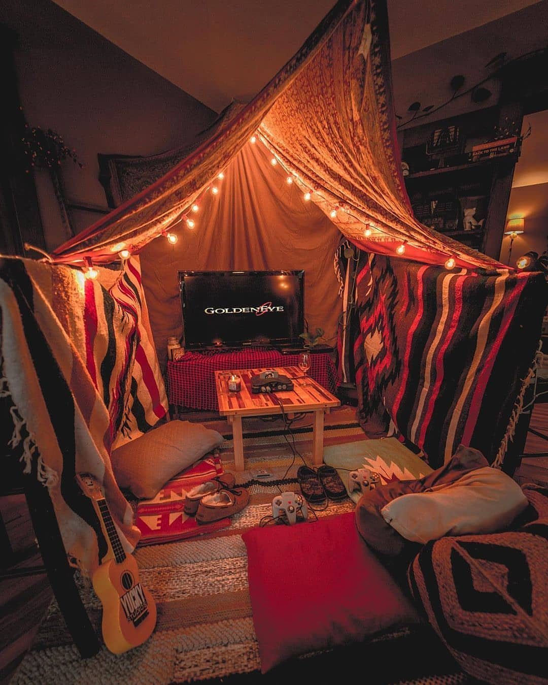 Cozy indoor blanket fort with string lights, pillows, a guitar, and a television.