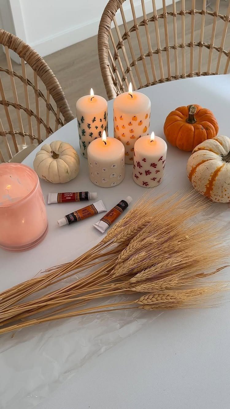 Painted autumn pillar candles and pumpkins with paint tubes on a white table.