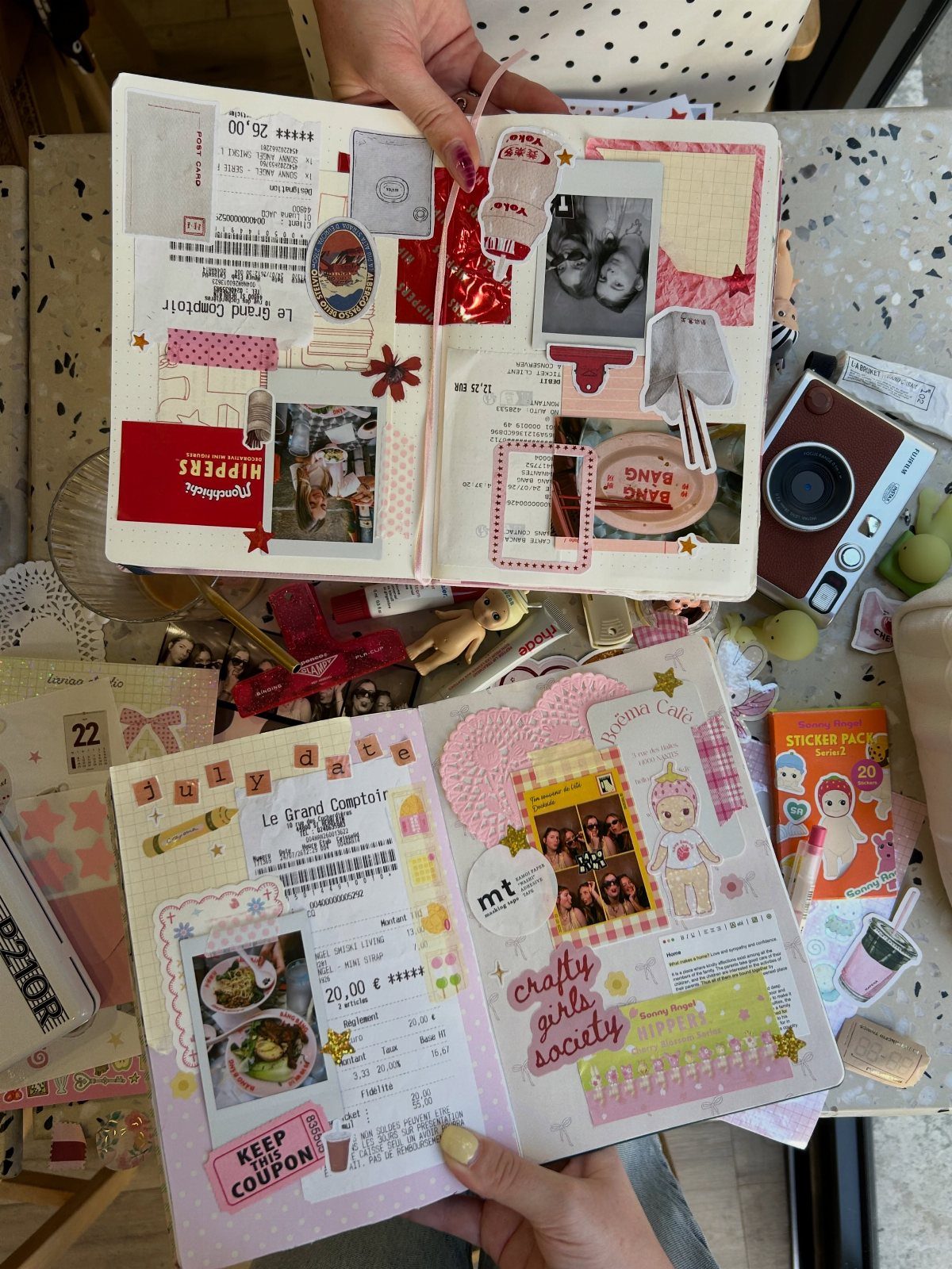 Open scrapbooks with photos and stickers held by hands on a craft table