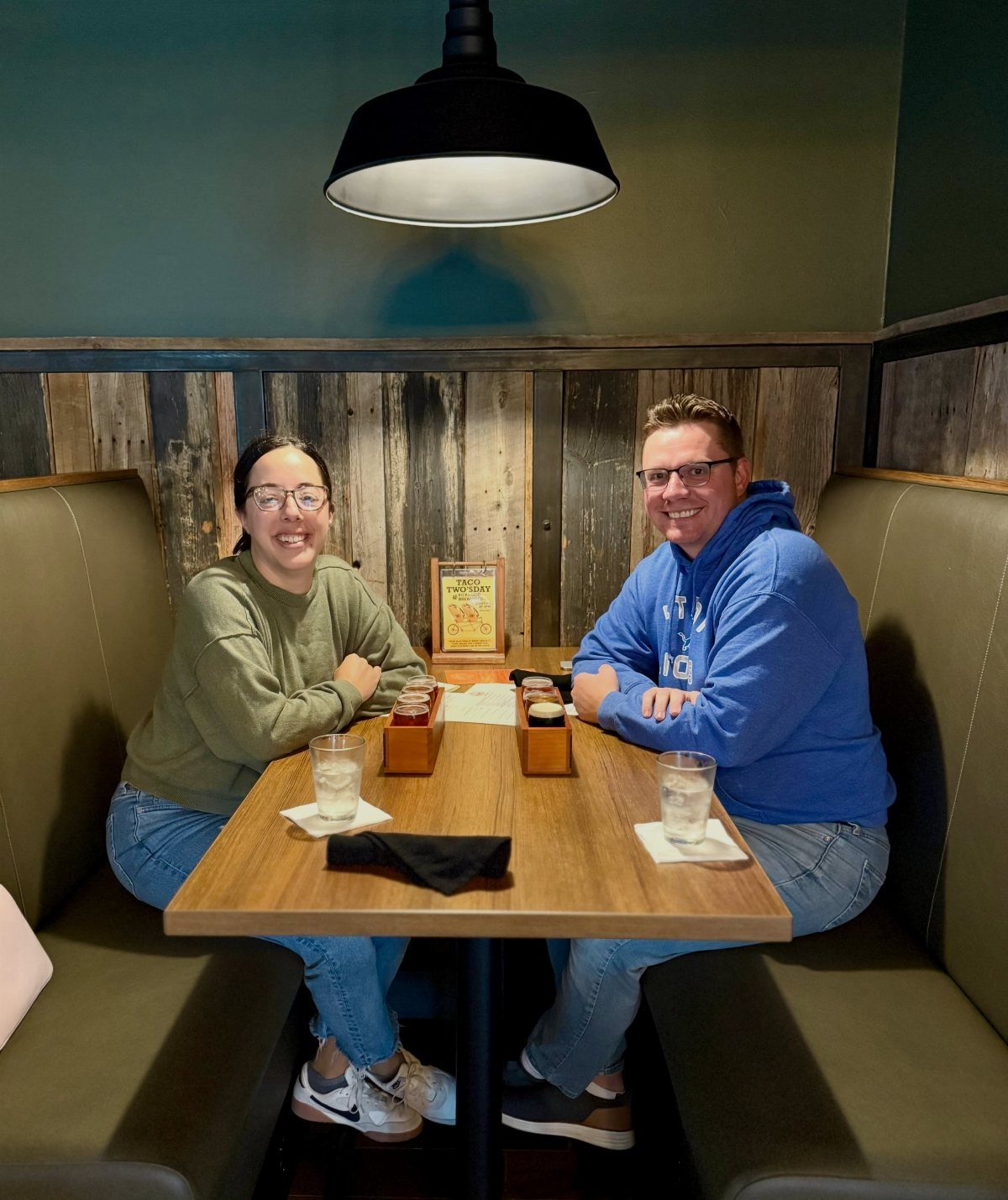 Couple smiling in a booth with beer tasting flights on a wooden table