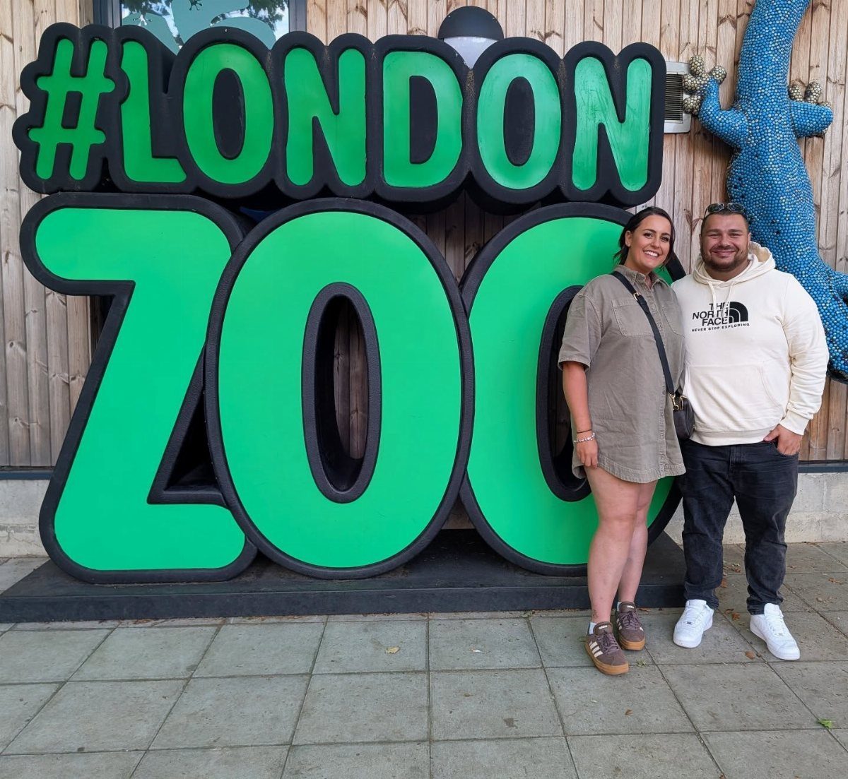Couple posing in front of a large green London Zoo sign outdoors.