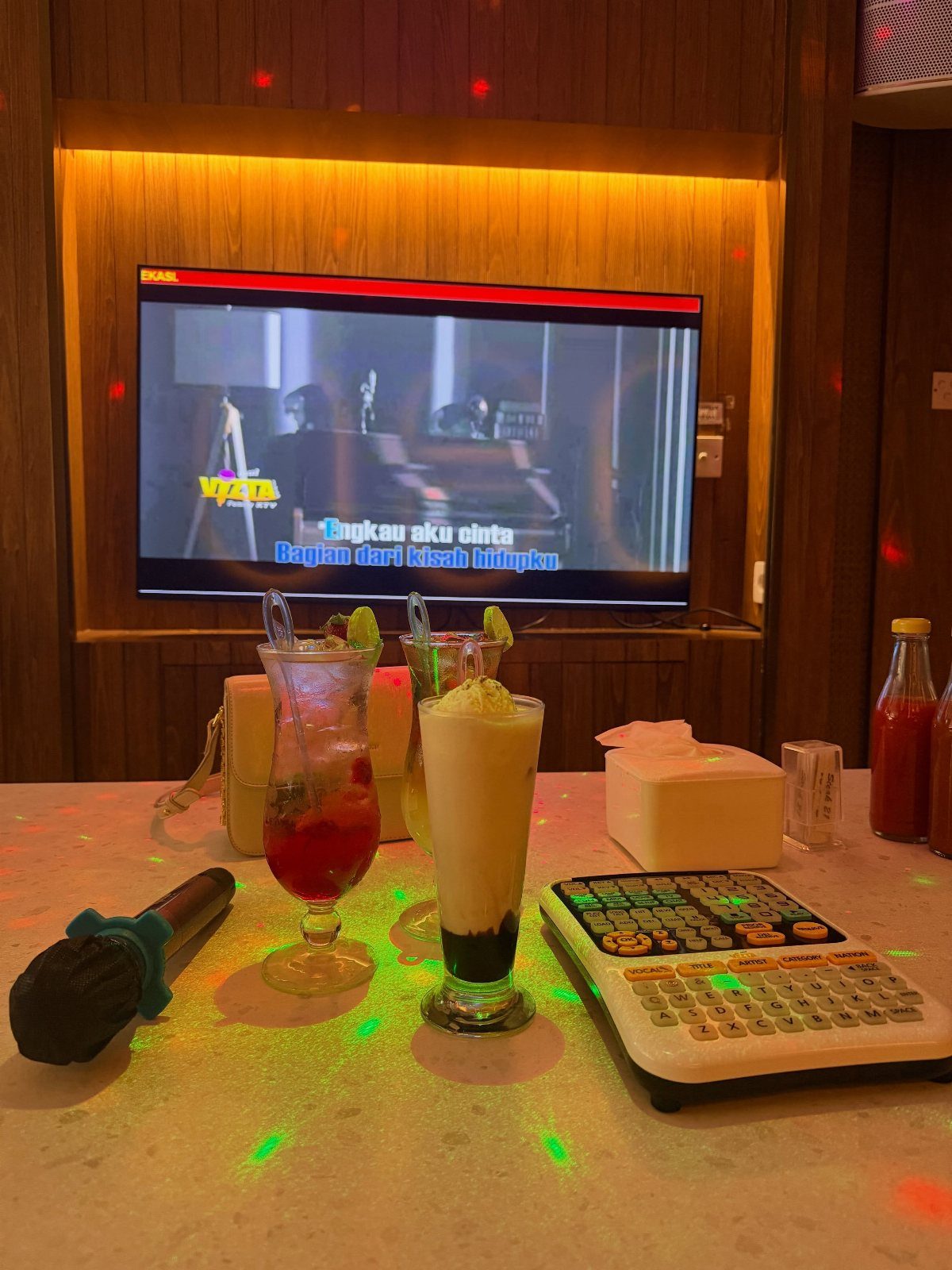 Karaoke microphone, song keyboard, and cocktails in a room with disco lights.
