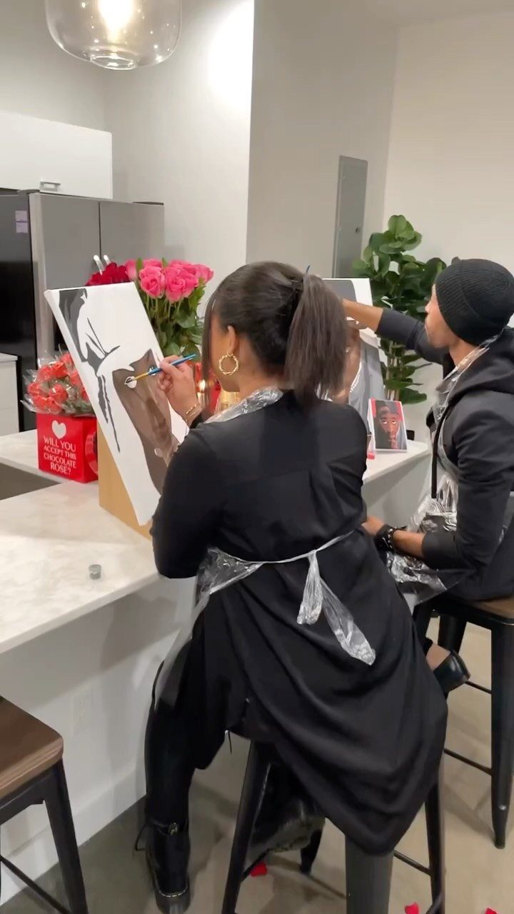 Two people painting on canvases while sitting at a white kitchen counter.