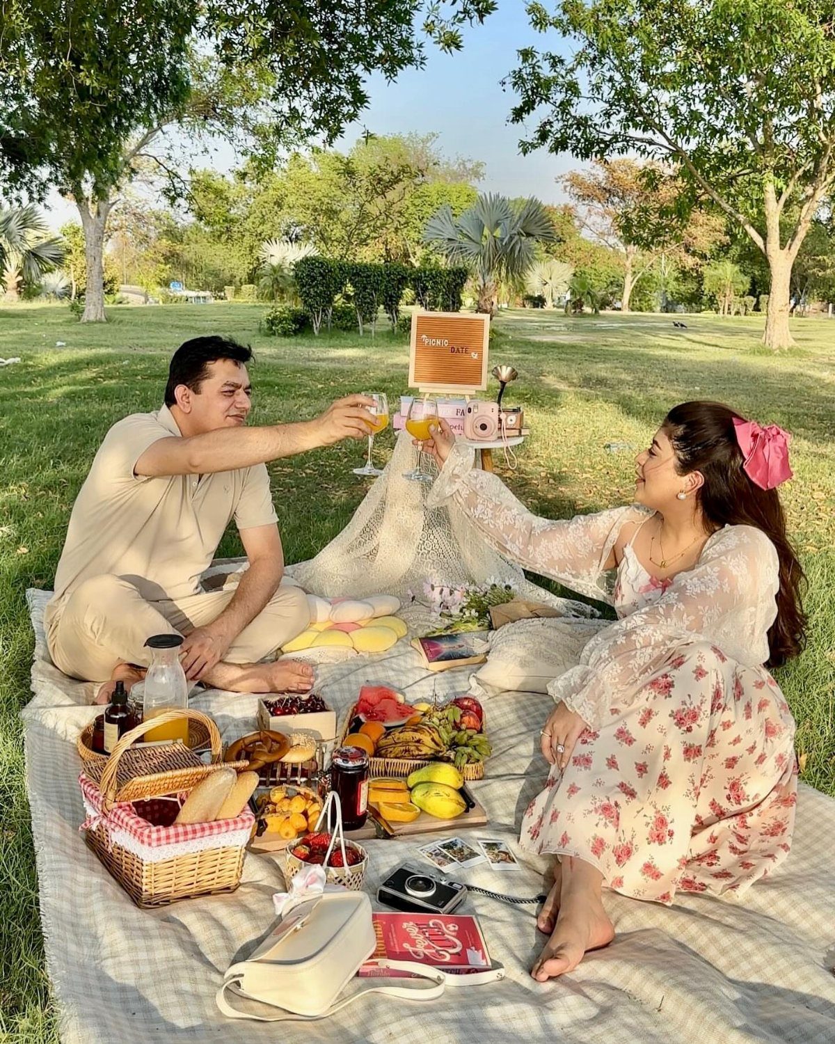 Couple clinking glasses during a picnic with food on a blanket in a park