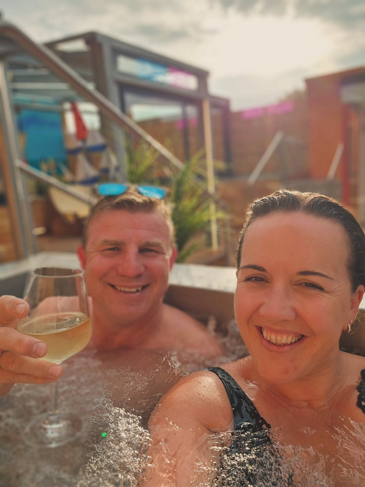 Smiling couple relaxing in a bubbling hot tub with a glass of white wine.