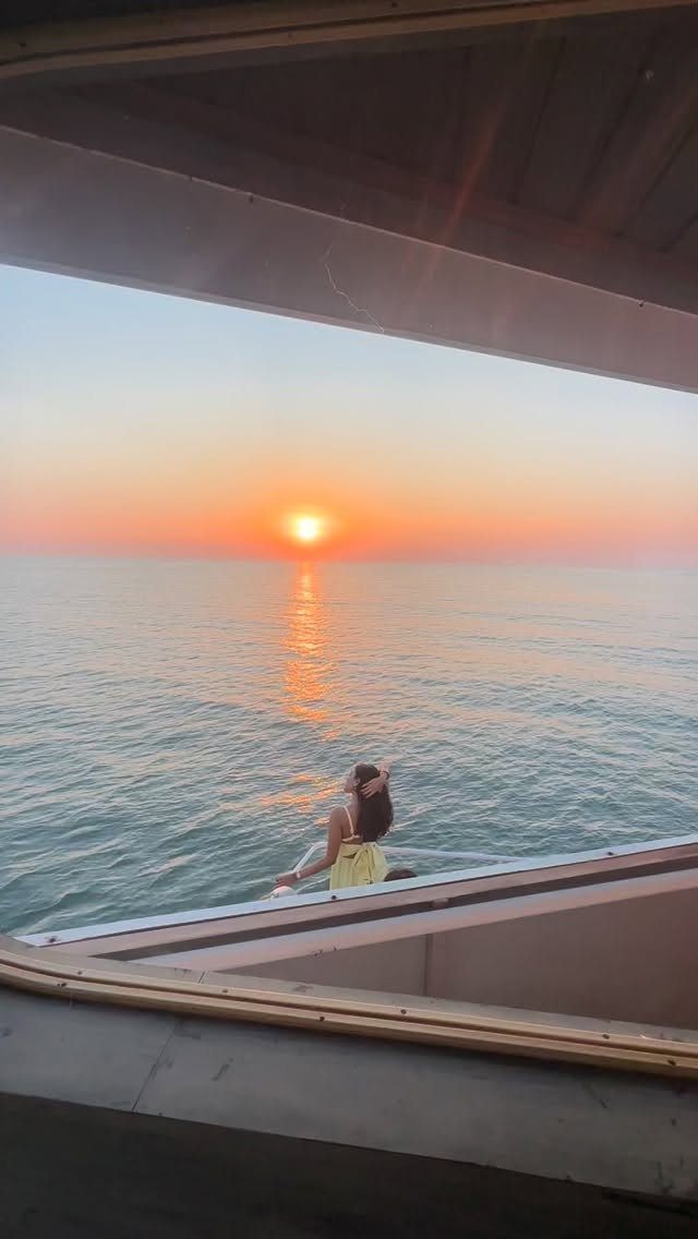 Woman in yellow dress on a boat deck watching a vibrant ocean sunset.