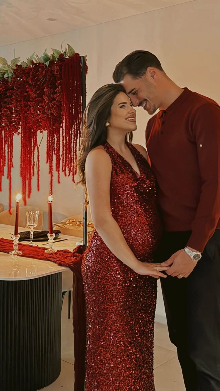 Couple in red clothing posing by a romantic dinner table with red decorations.