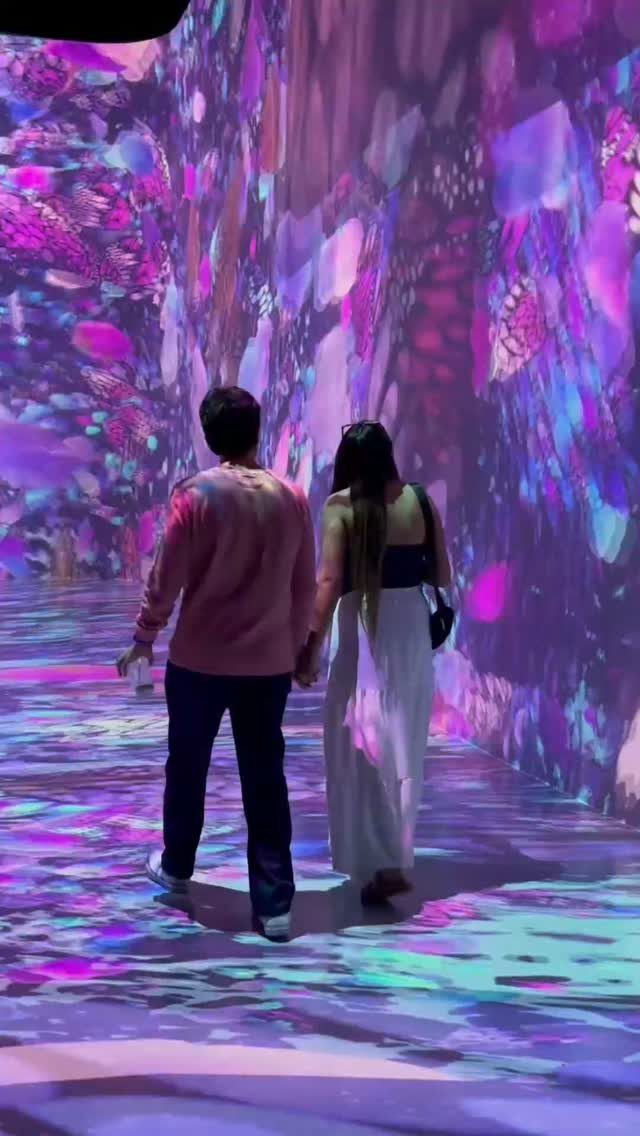 Couple holding hands walking through a colorful immersive digital art museum exhibit.