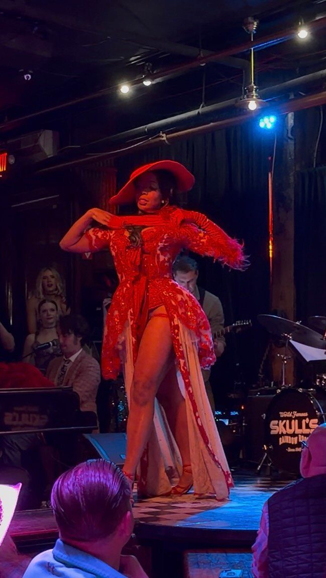 Performer in red lace outfit and hat performing on a stage in a club