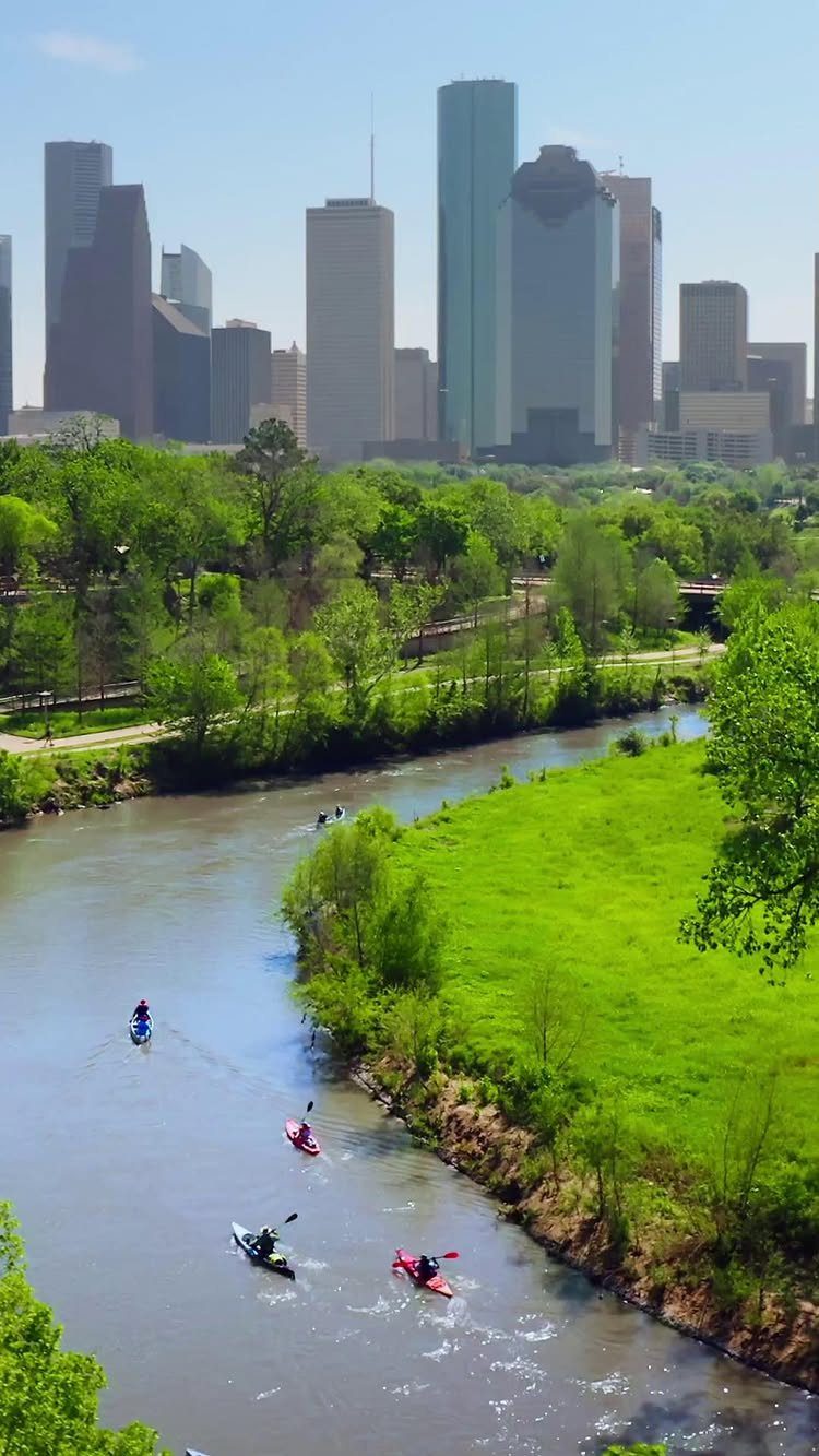 Kayakers paddling down a river with a city skyline in the background.