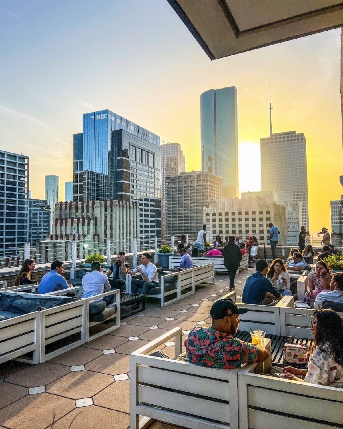 People relaxing on a rooftop terrace overlooking a city skyline at sunset.