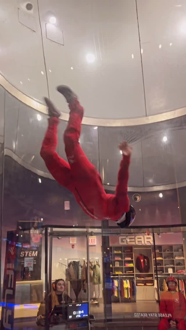 Person in red jumpsuit floating upside down in an indoor skydiving wind tunnel