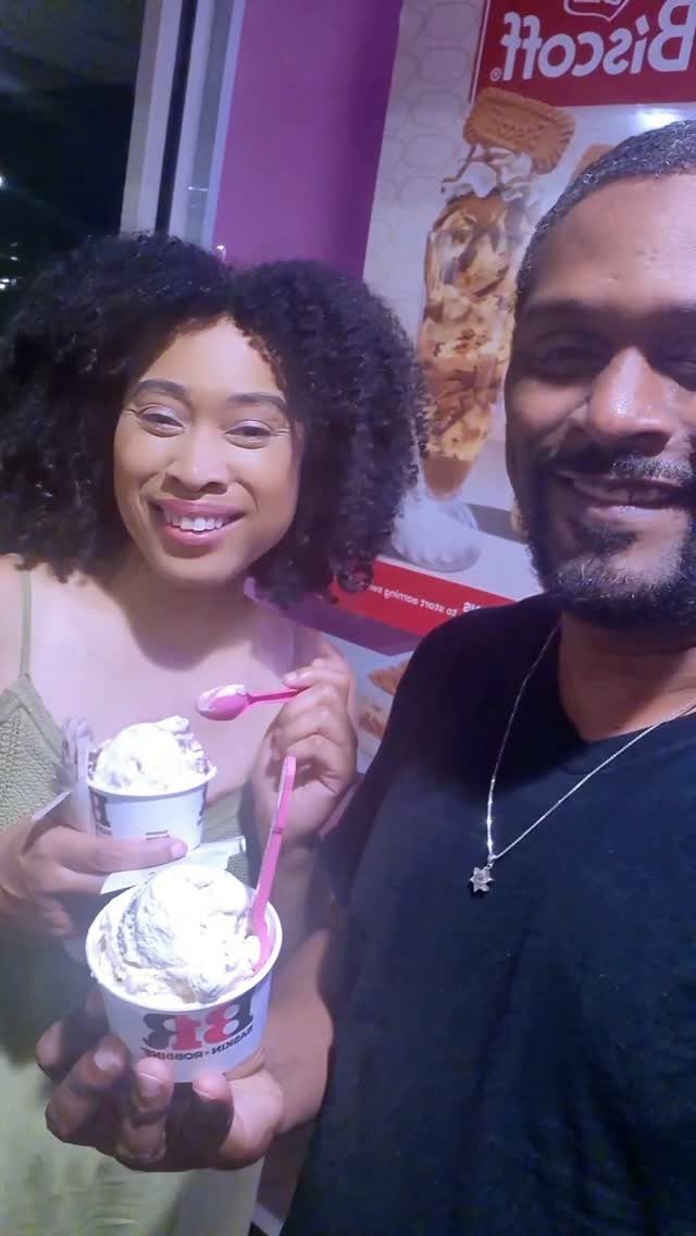 Smiling couple holding cups of white ice cream in front of a purple sign.