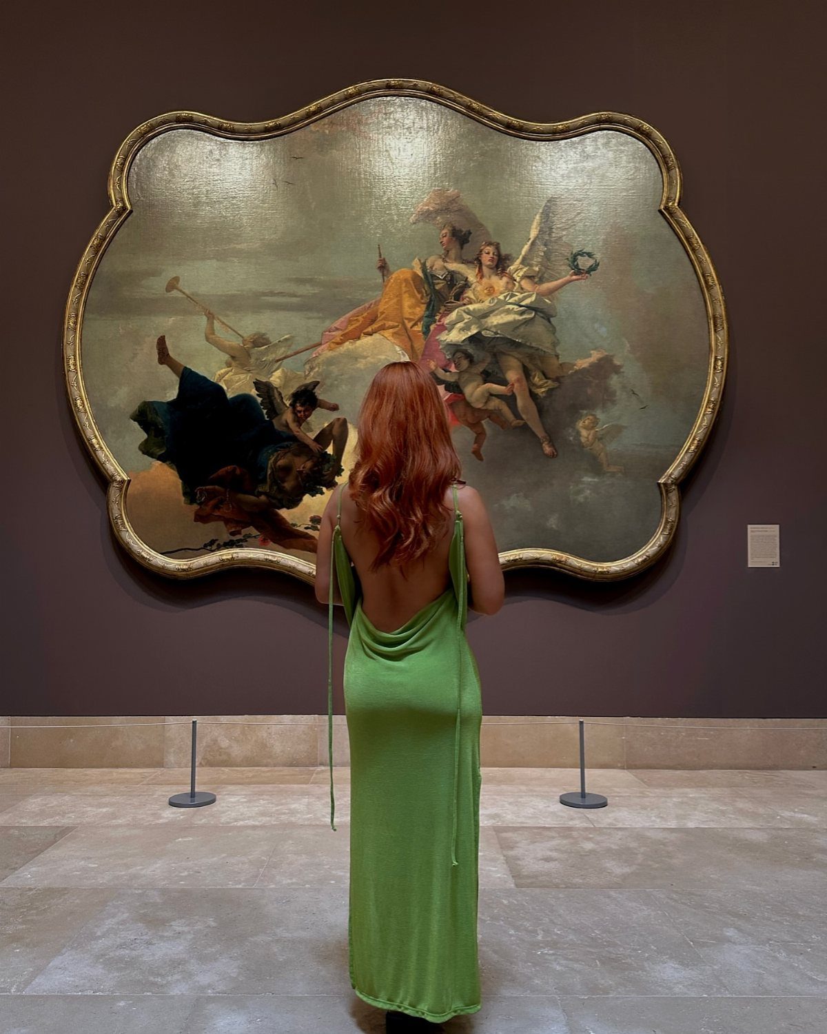 Woman in green dress viewing a large classical painting in an art museum