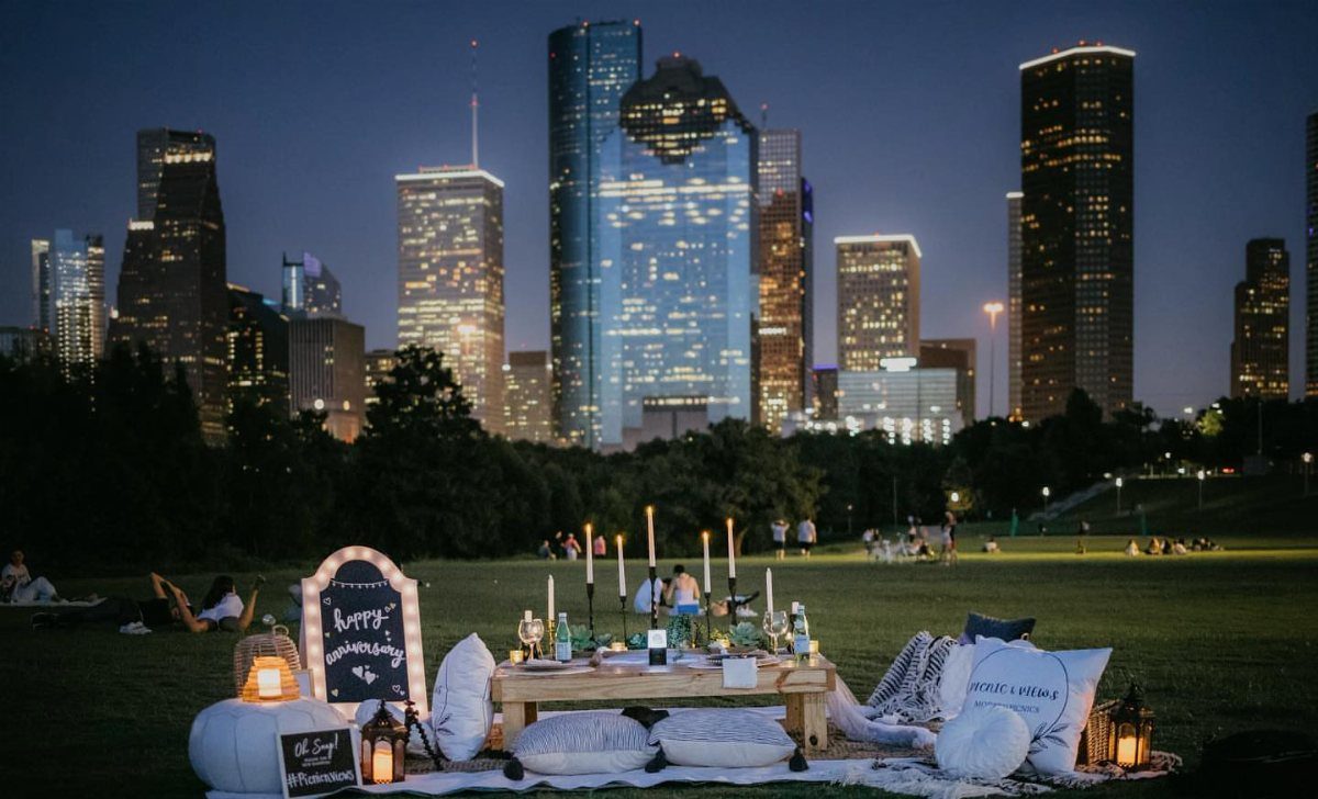 Luxury picnic setup with candles and pillows in a park facing a city skyline