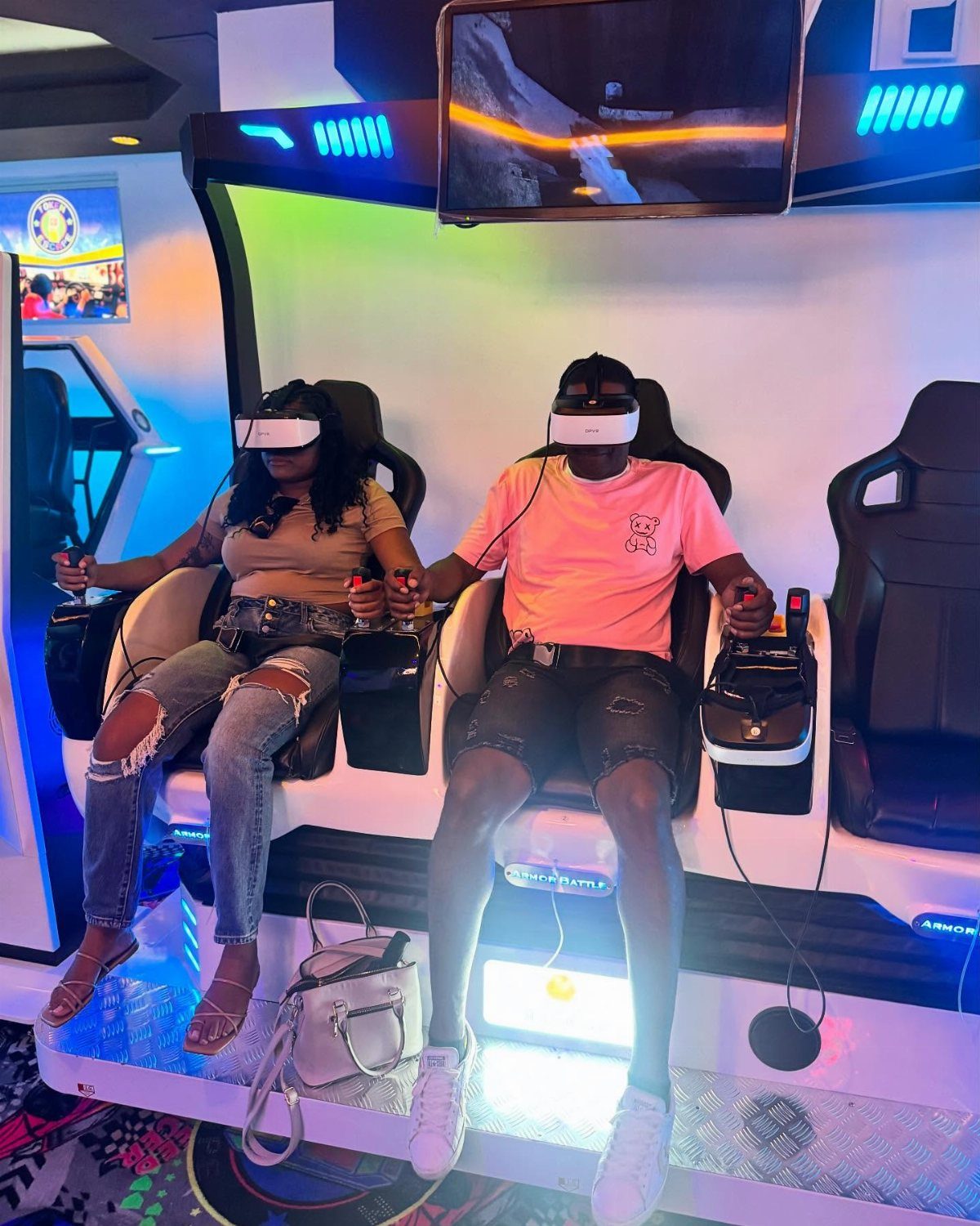 Man and woman wearing VR headsets while sitting in gaming chairs at an arcade.