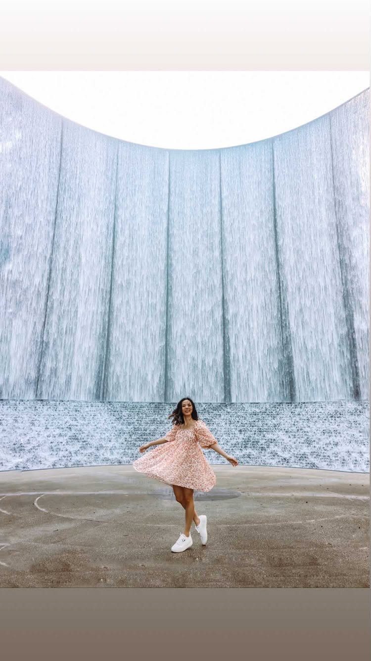Woman in pink dress posing before the curved Waterwall Park waterfall in Houston.