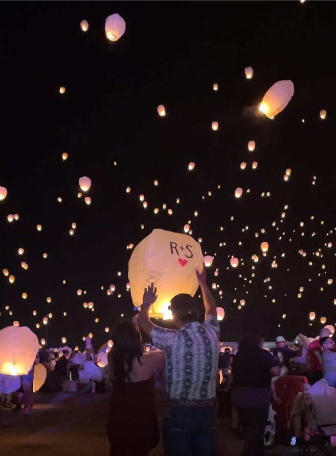 Couple releasing a glowing paper lantern into a night sky filled with lanterns.