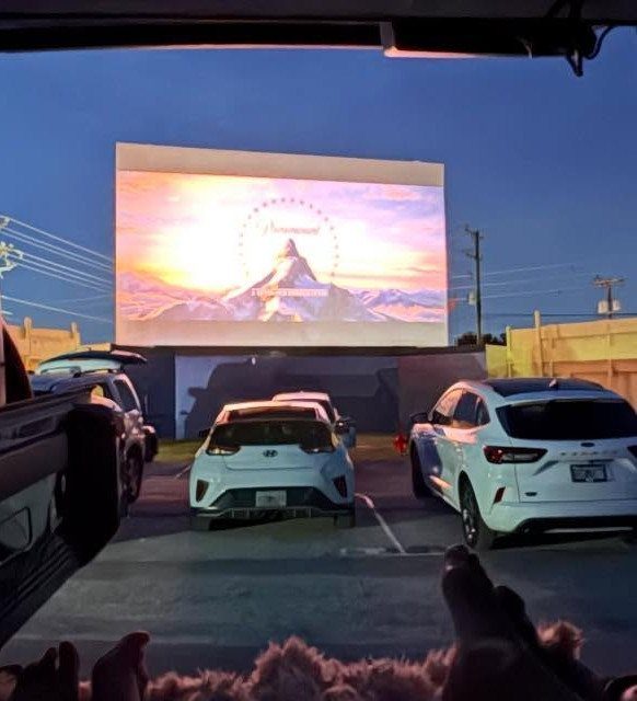 Outdoor movie screen showing a mountain scene with cars parked in front.