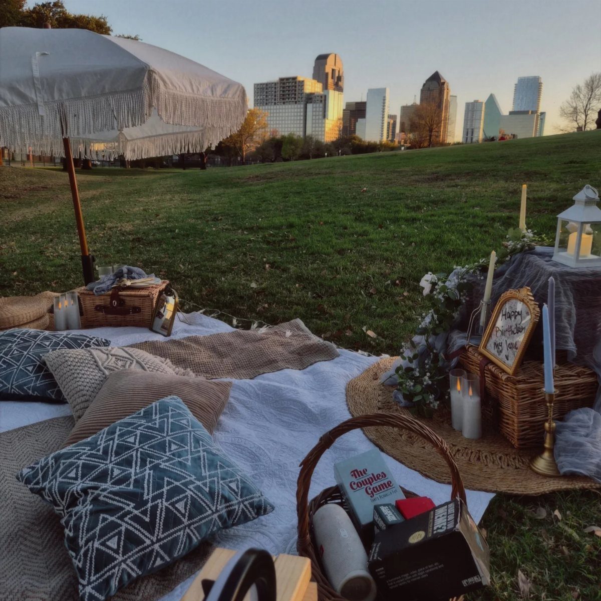 Romantic picnic setup with pillows and candles on a hill overlooking a city skyline.