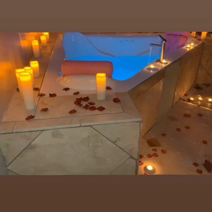 Bathtub with blue water, lit candles, and red rose petals for a romantic evening.