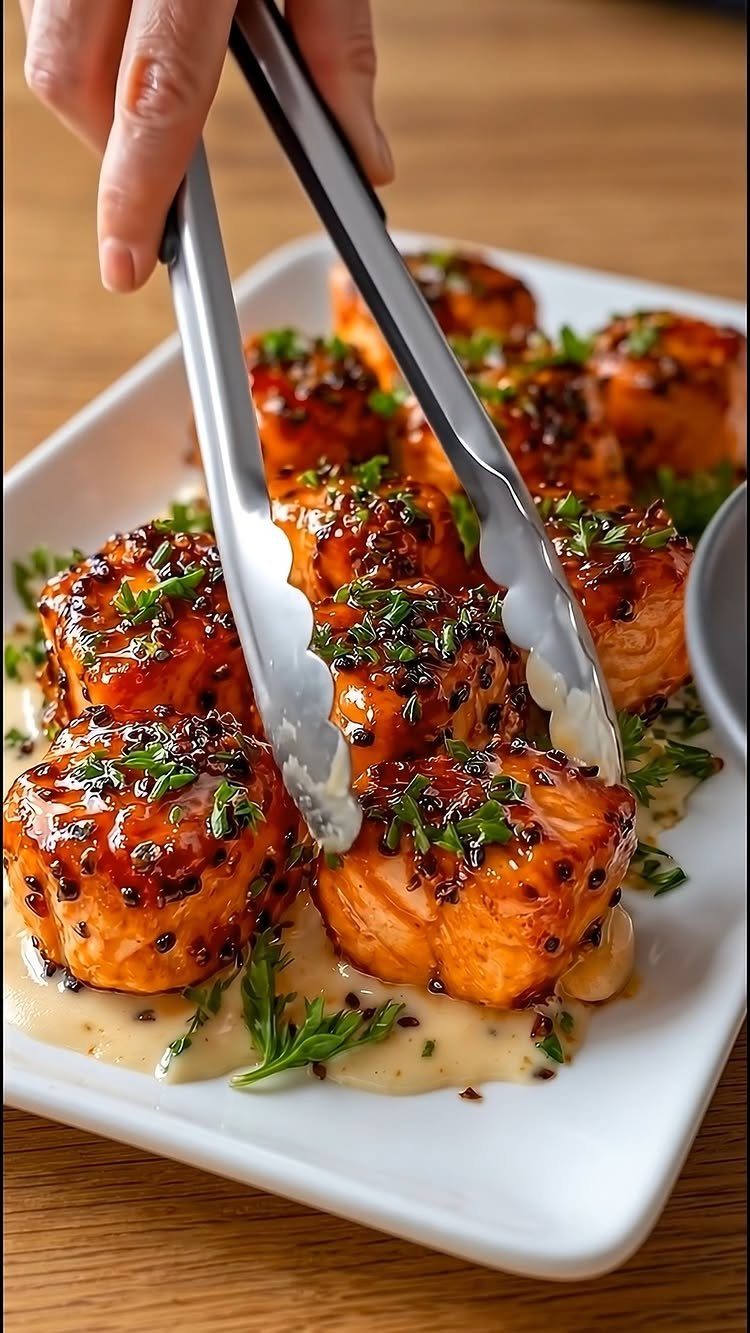Glazed salmon cubes with sesame seeds and herbs on a white plate.