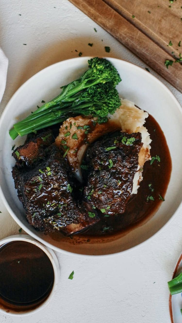 Braised short ribs with mashed potatoes and broccolini on a white plate.