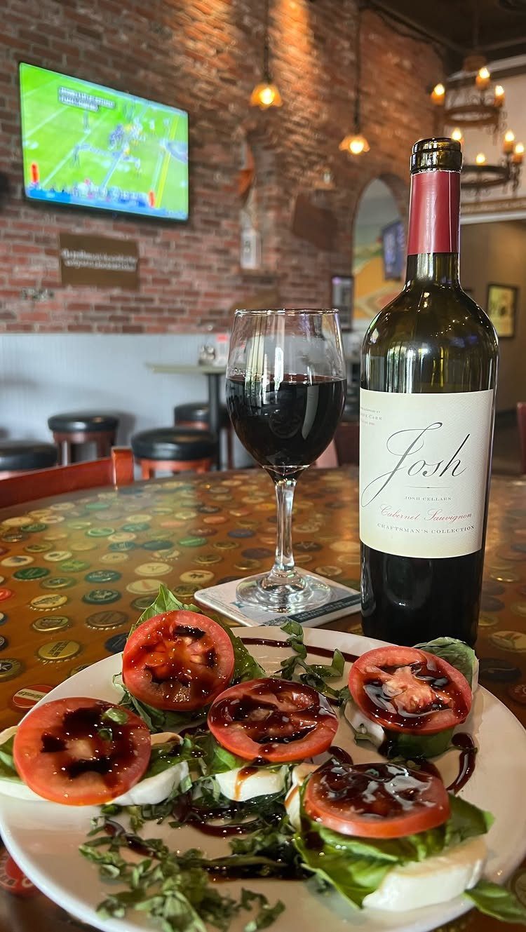 Caprese salad with tomato, mozzarella, and balsamic glaze next to red wine.
