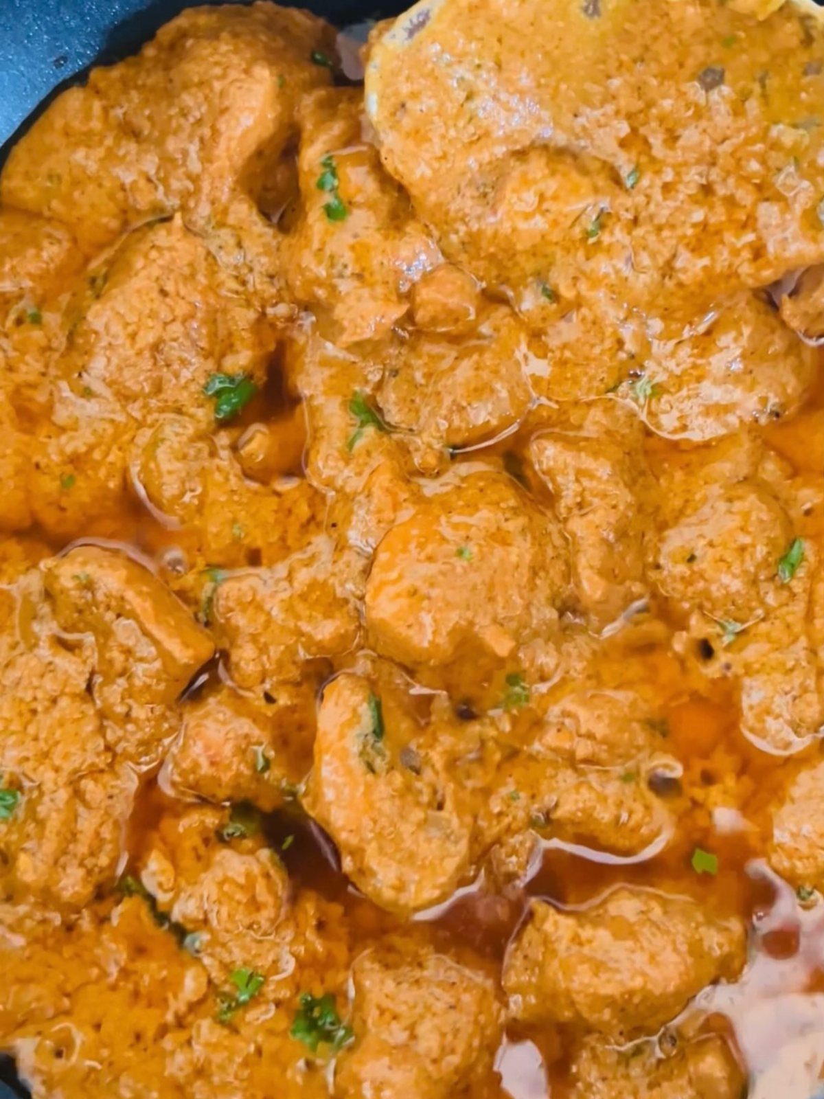 Chicken korma curry with a rich orange sauce and green herbs in a pan.