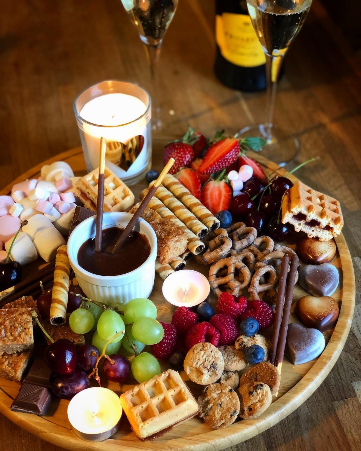 Chocolate fondue platter with fresh fruits, waffles, and sweets with champagne glasses.