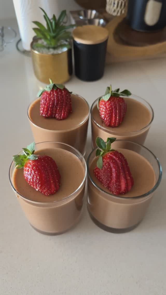 Chocolate mousse in four glass cups topped with fresh red strawberries on white counter