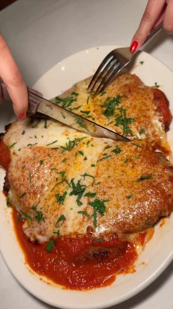 Breaded veal parmesan with melted cheese and tomato sauce being cut with cutlery.