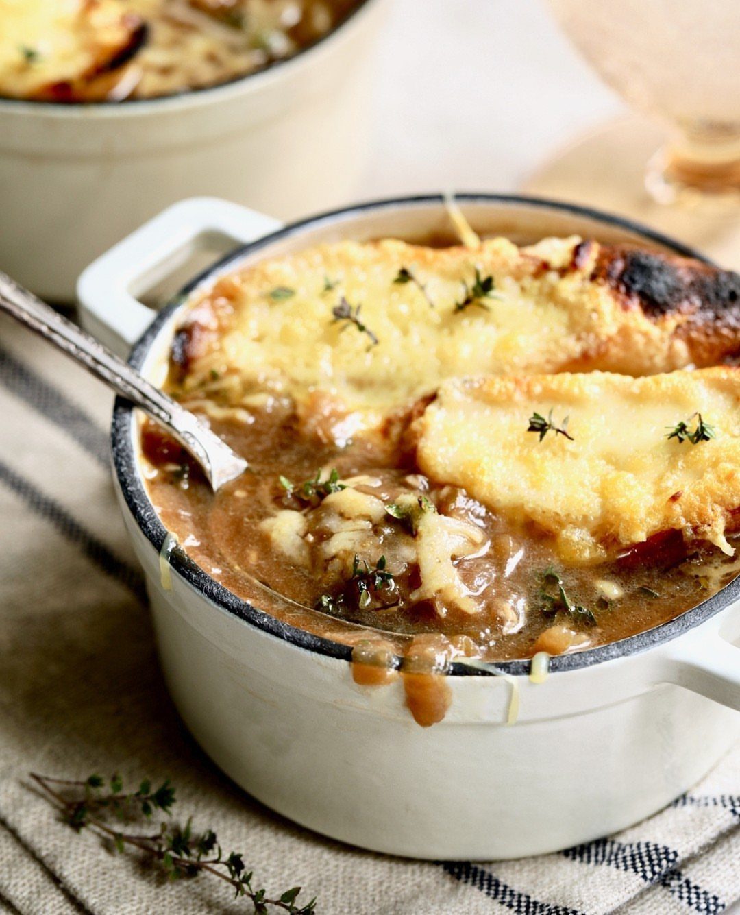 French onion soup in white crocks with melted cheese and fresh thyme garnish.