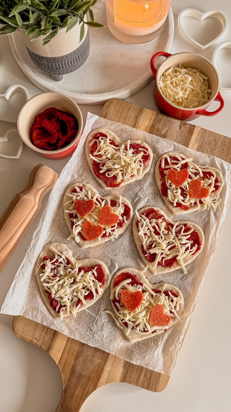 Heart-shaped mini pizzas with cheese and pepperoni on a wooden cutting board.