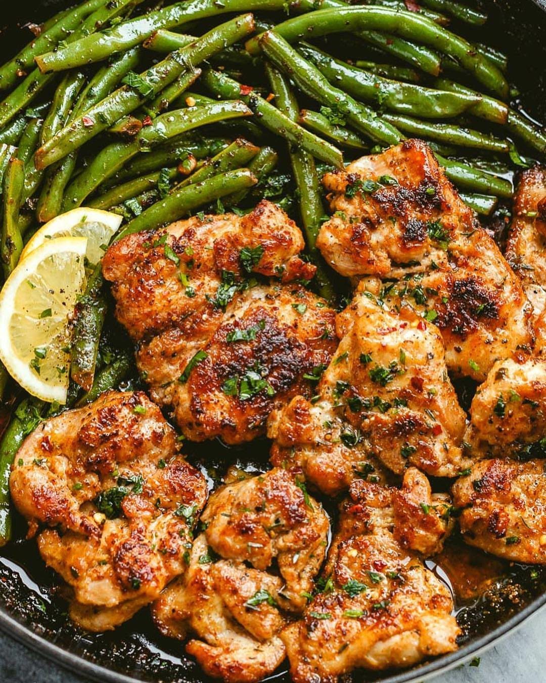 Seared chicken thighs with green beans and lemon slices in a black skillet.